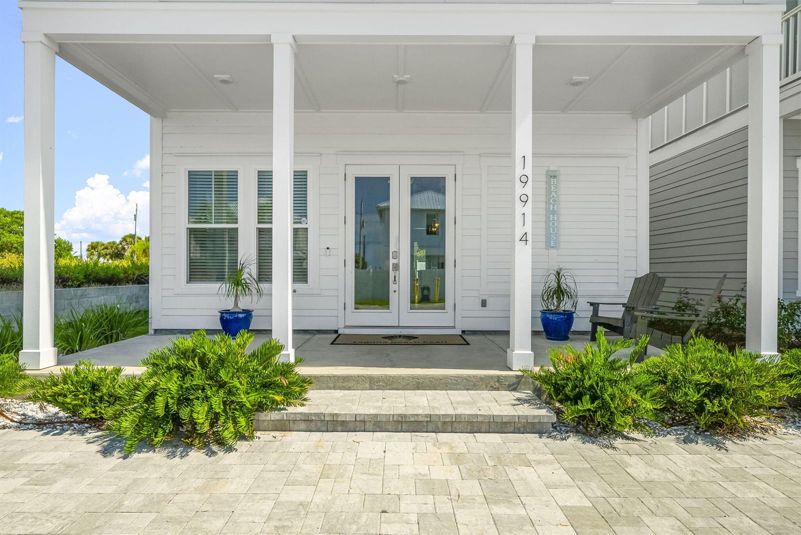 A white house exterior features a covered porch, double glass front doors, and potted plants — 19914 Front Beach Road, FL 32413, FL