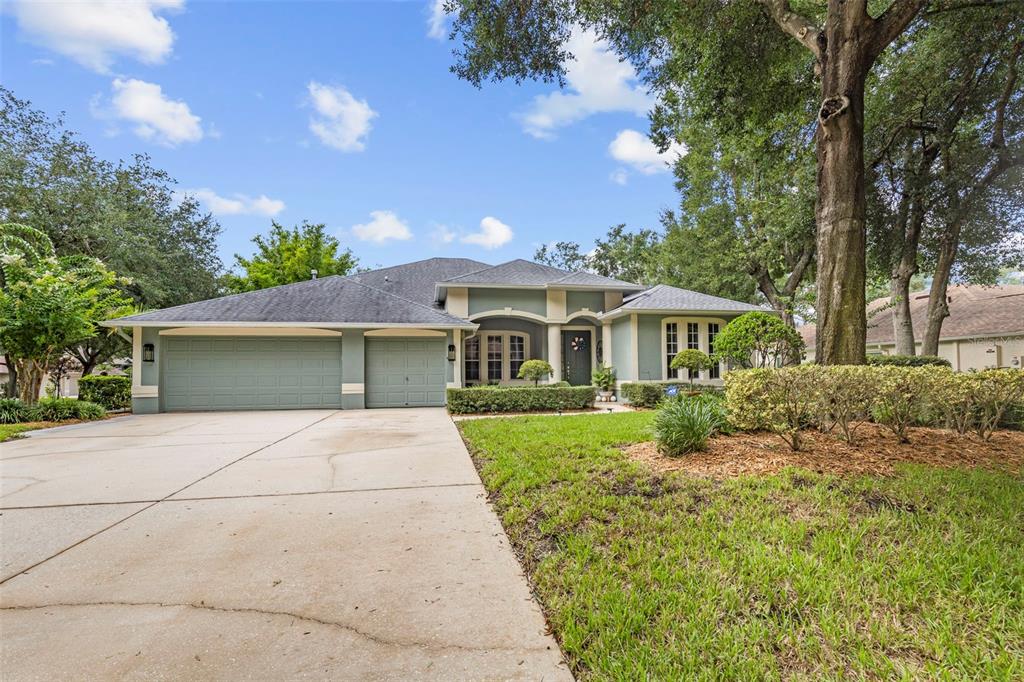 A single-story house with a three-car garage, light green siding, and a concrete driveway — 28 CAMELOT RIDGE DRIVE, BRANDON, FL
