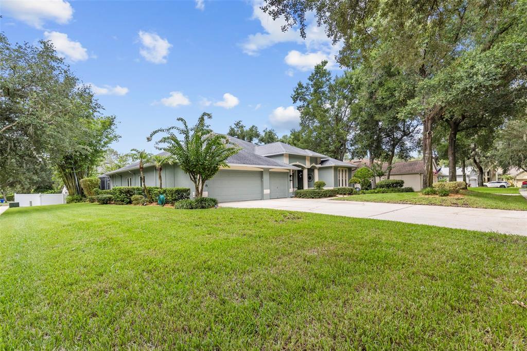 A single-story house with a multi-car garage and a large front lawn under mature trees — 28 CAMELOT RIDGE DRIVE, BRANDON, FL