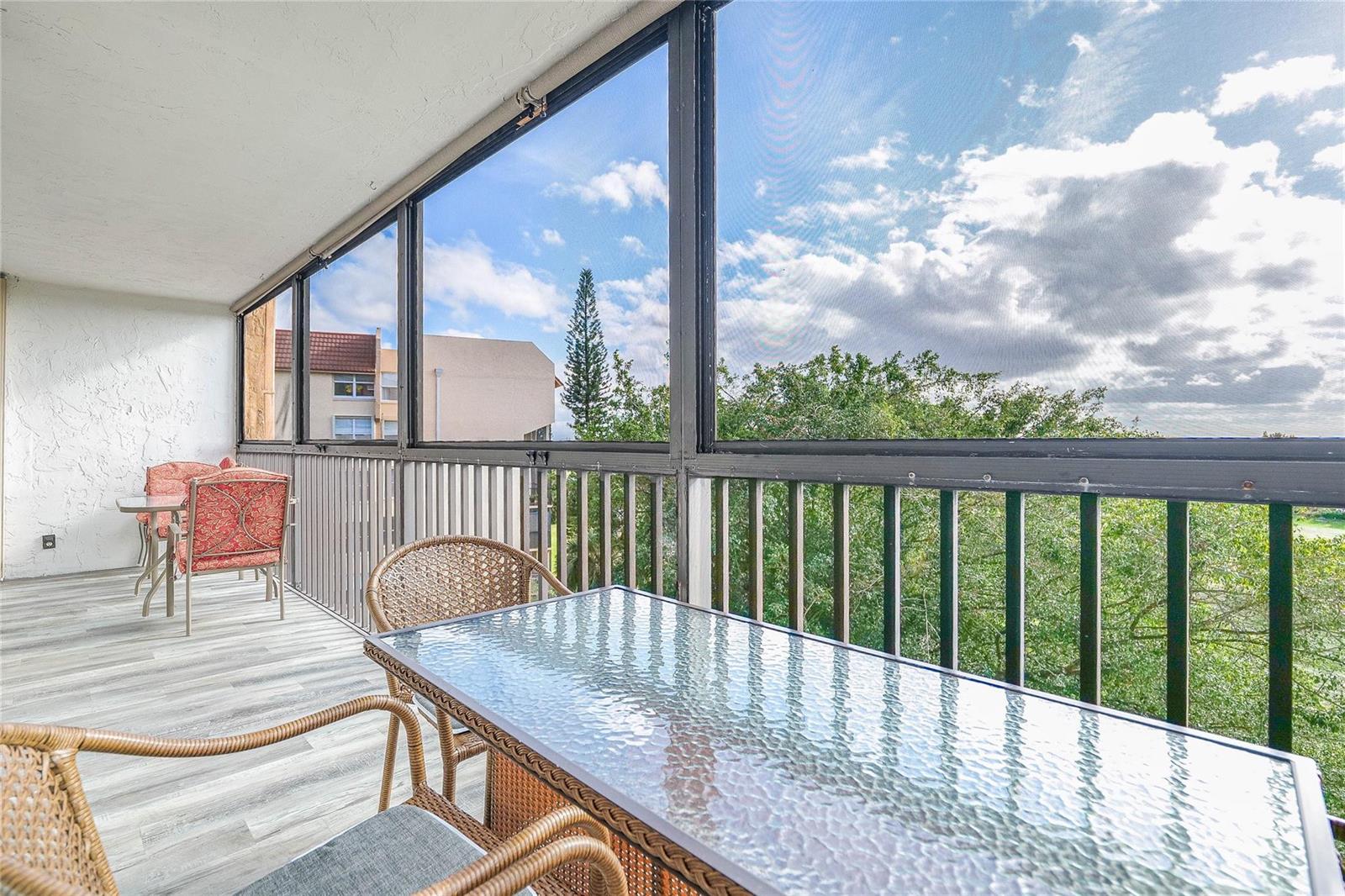 A screened-in balcony features a glass-topped table, wicker chairs, and a view of trees — 3821 Environ Boulevard # 603, Lauderhill FL 33319, LAUDERHILL, FL