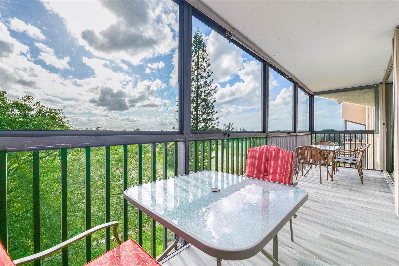 A screened-in balcony features a glass-top table, red-cushioned chairs, and views of trees and sky — 3821 Environ Boulevard # 603, Lauderhill FL 33319, LAUDERHILL, FL