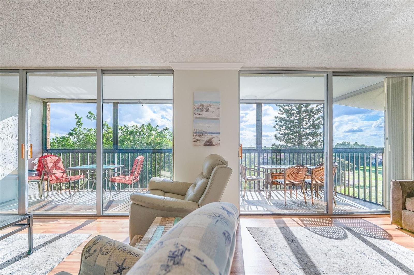 A living room with a light-colored recliner and sofa opens to a balcony with outdoor furniture — 3821 Environ Boulevard # 603, Lauderhill FL 33319, LAUDERHILL, FL
