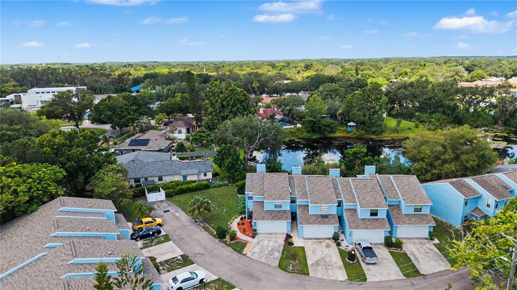 An aerial view shows several light blue townhouses with shingled roofs near a small pond — 13302 ARENA PLACE UNIT E, TAMPA, FL
