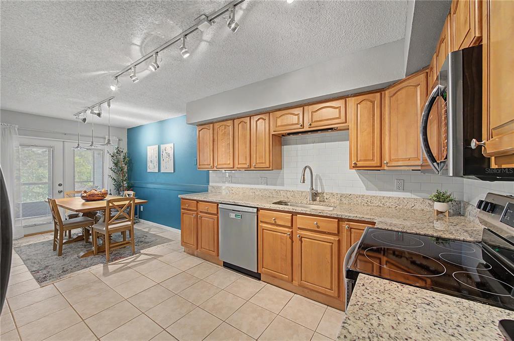A kitchen with wood cabinets, granite countertops, and a dining area with a blue wall — 13302 ARENA PLACE UNIT E, TAMPA, FL