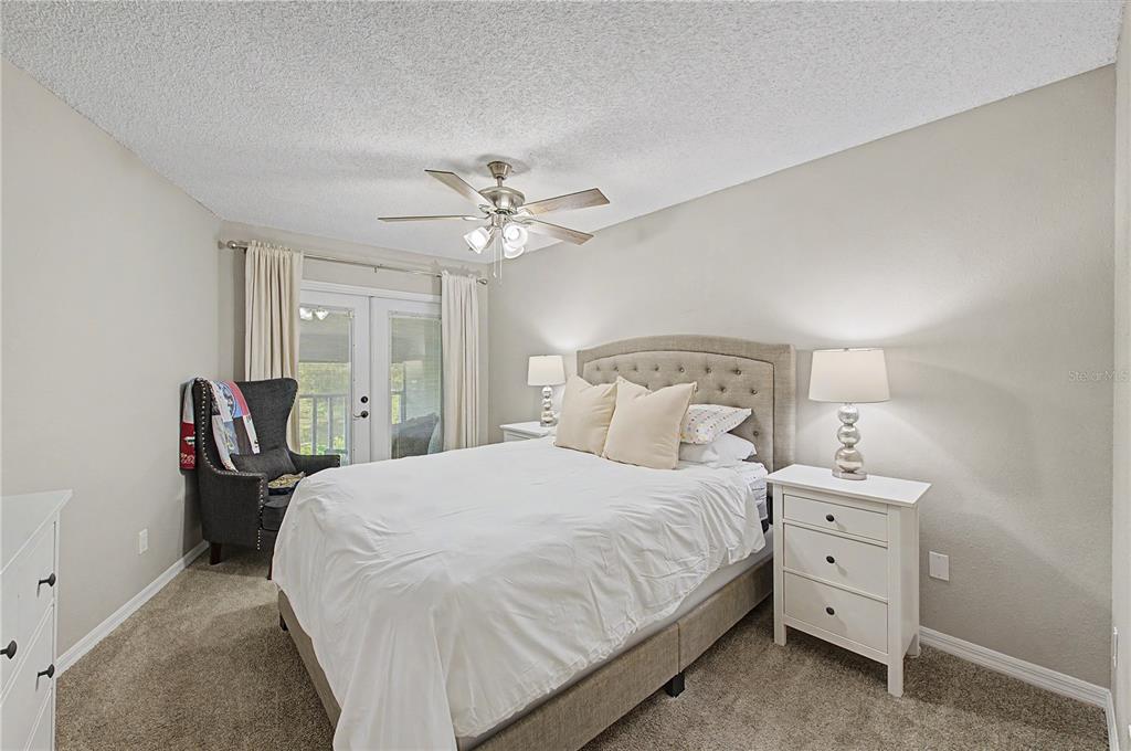 A bedroom features a tufted headboard, white bedding, two nightstands, and a dark armchair — 13302 ARENA PLACE UNIT E, TAMPA, FL