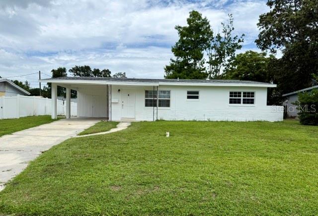A white, single-story house with a carport sits on a grassy lawn under a cloudy sky — 10450 EASTSIDE AVENUE, BROOKSVILLE, FL