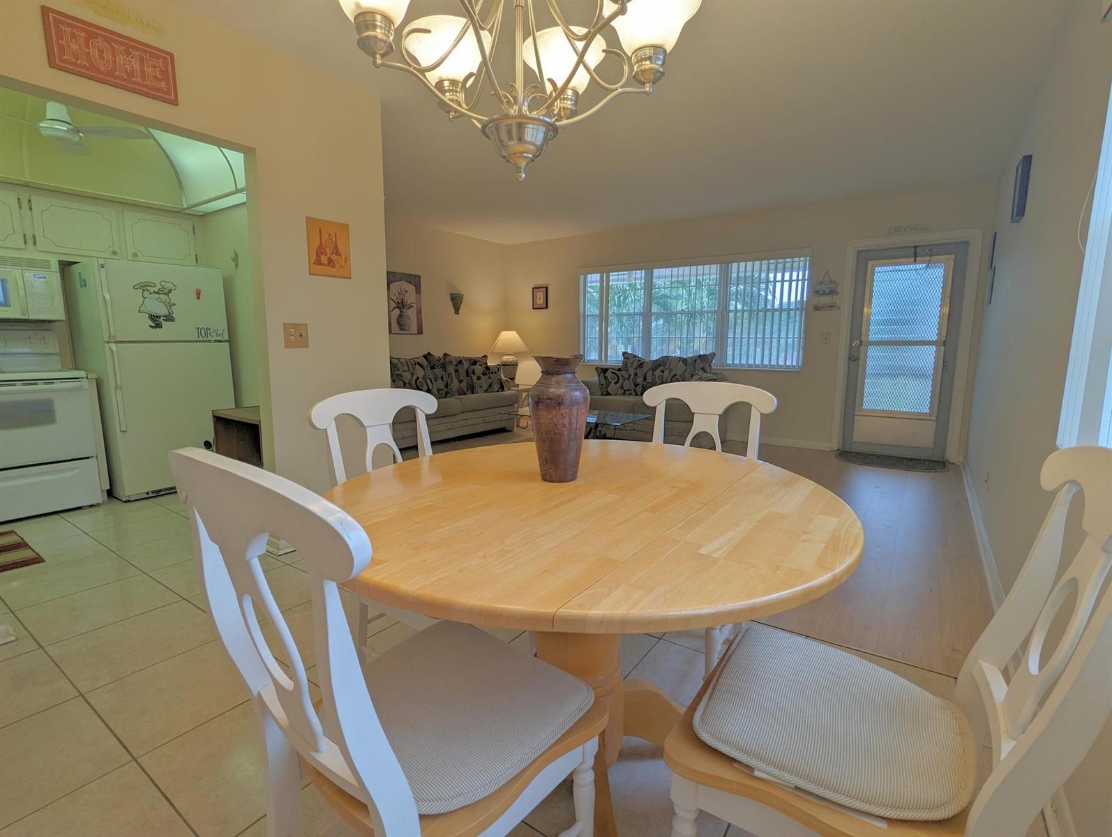 A dining area with a round wooden table and white chairs sits before a living room — 113 E Waltham E, West Palm Beach FL 33417, WEST PALM BEACH, FL