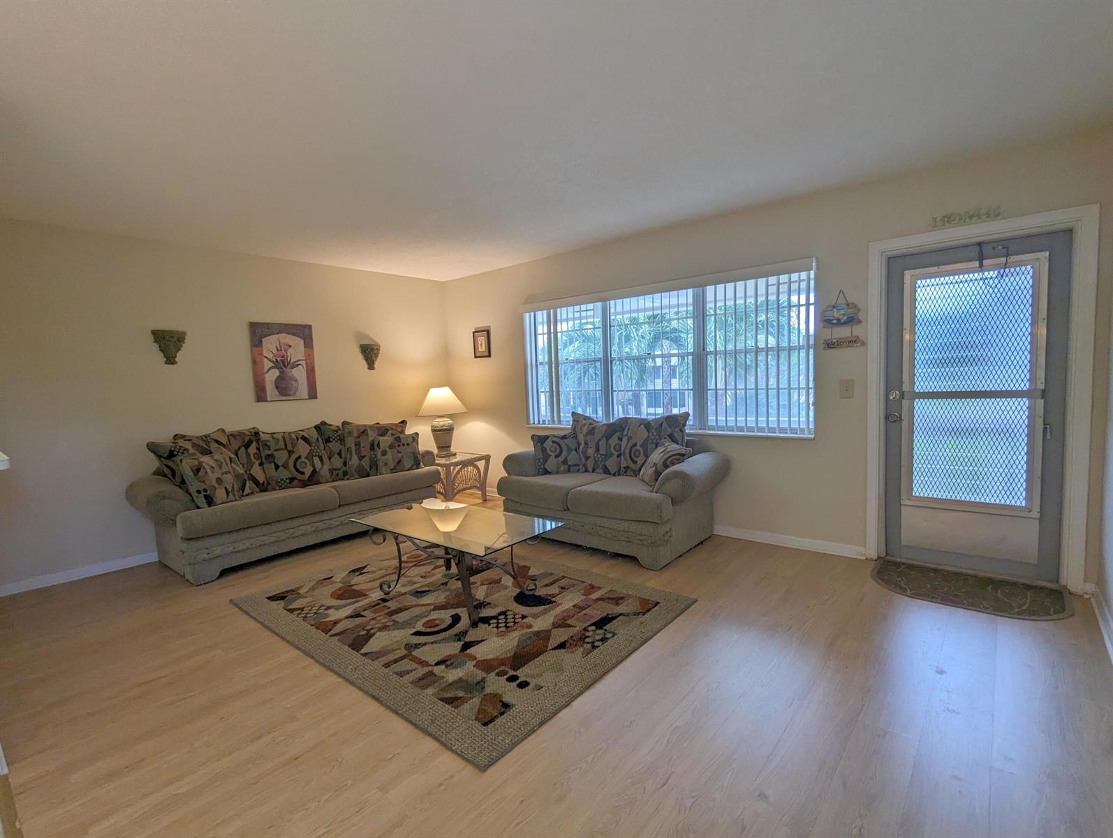 A living room features light wood flooring, two fabric sofas, a glass coffee table, and windows — 113 E Waltham E, West Palm Beach FL 33417, WEST PALM BEACH, FL