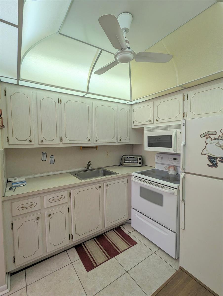 A small kitchen with white cabinets, white appliances, tile flooring, and a vaulted ceiling — 113 E Waltham E, West Palm Beach FL 33417, WEST PALM BEACH, FL