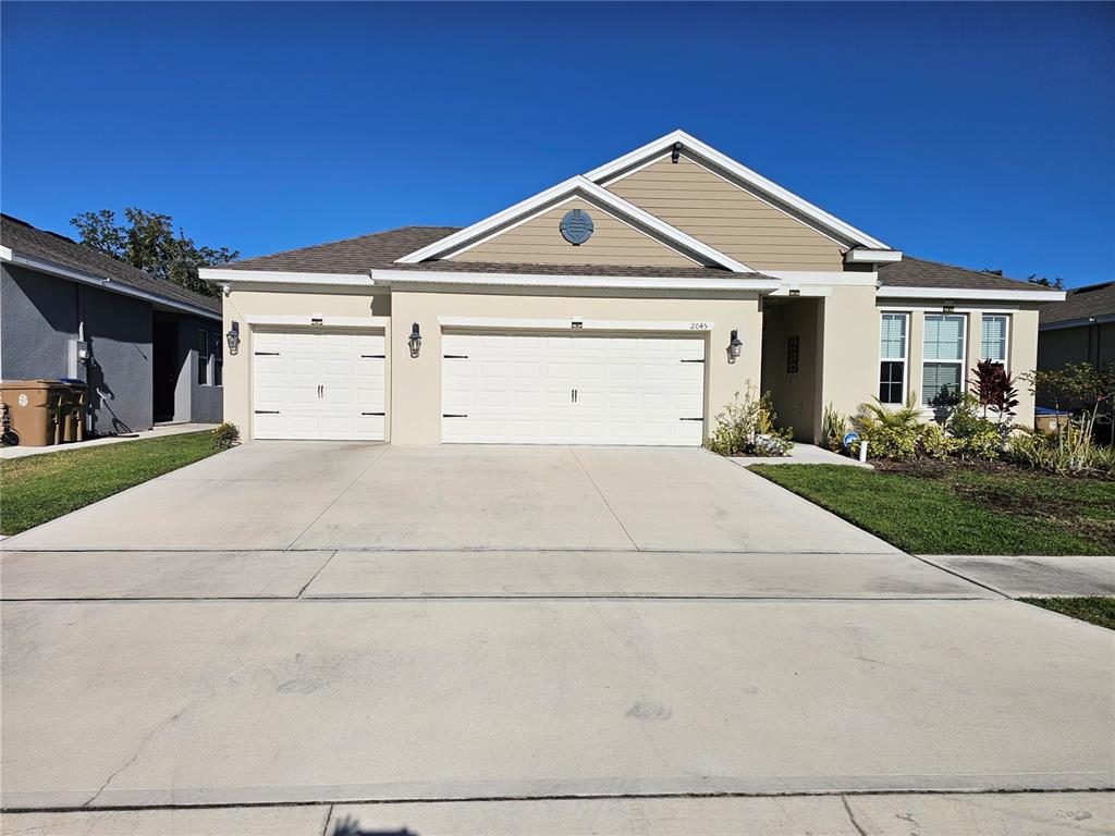 A beige single-story house features a three-car garage and a concrete driveway under a clear sky — 2045 RANKIN STREET, KISSIMMEE, FL