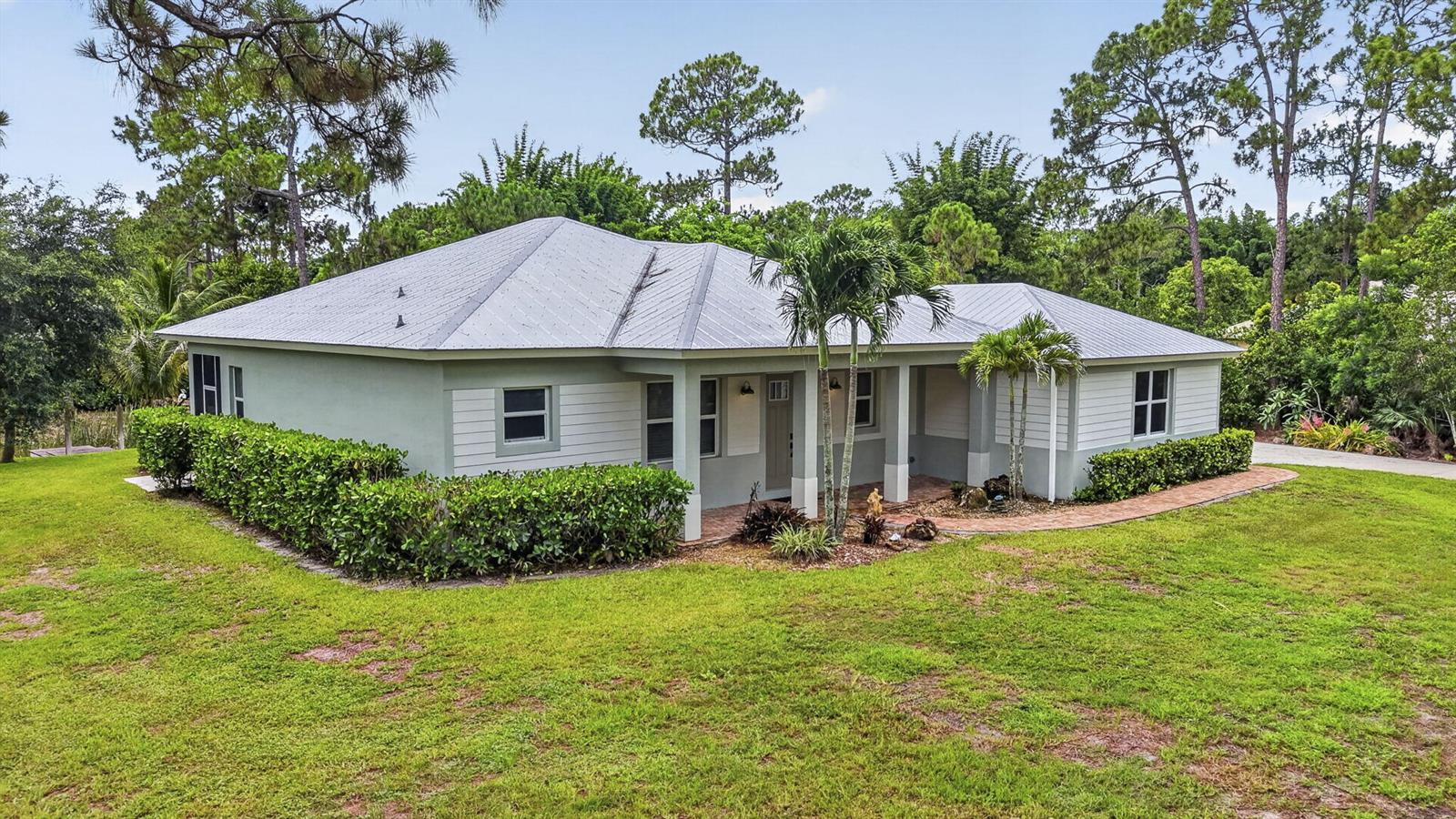 A single-story house with a metal roof, light-colored siding, and a brick walkway — 18842 93rd Road N, FL 33470, FL