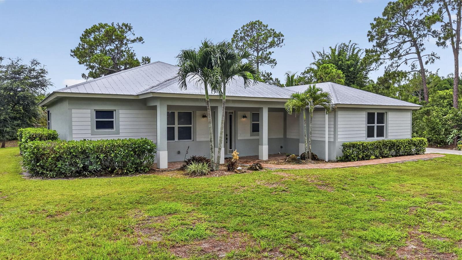 A single-story house with light gray siding, a metal roof, and a brick walkway — 18842 93rd Road N, FL 33470, FL