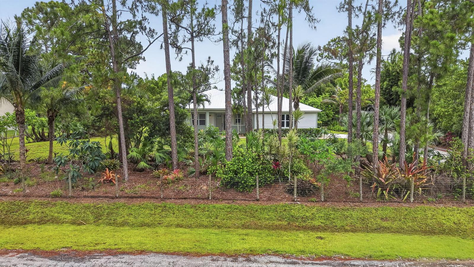 A single-story house with a white roof is partially obscured by trees and lush landscaping — 18842 93rd Road N, FL 33470, FL