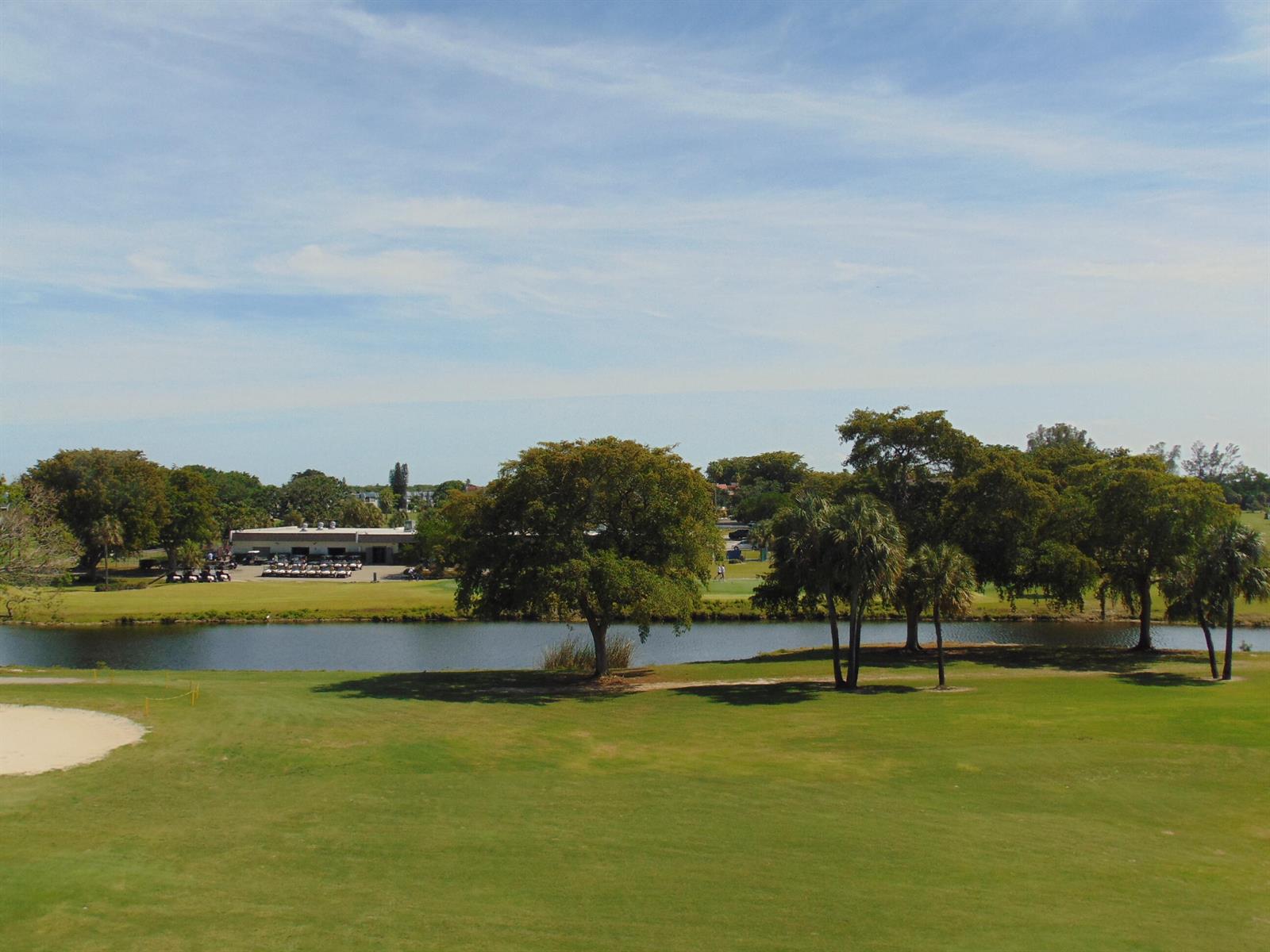 A view of a golf course with a pond, trees, and a clubhouse in the distance — 7640 NW 18th Street # 401, Margate FL 33063, MARGATE, FL