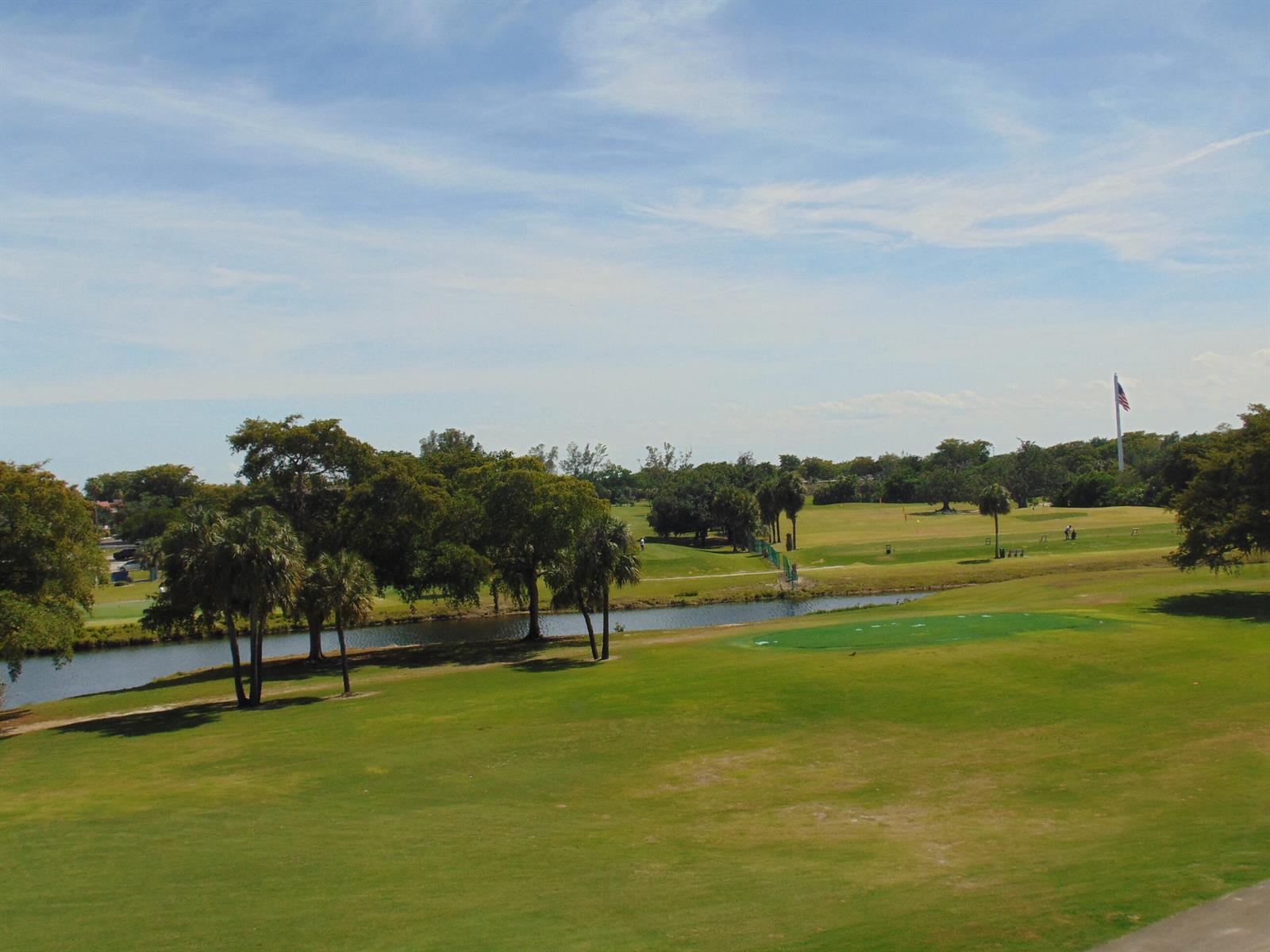 A view of a golf course with a pond, palm trees, and an American flag — 7640 NW 18th Street # 401, Margate FL 33063, MARGATE, FL
