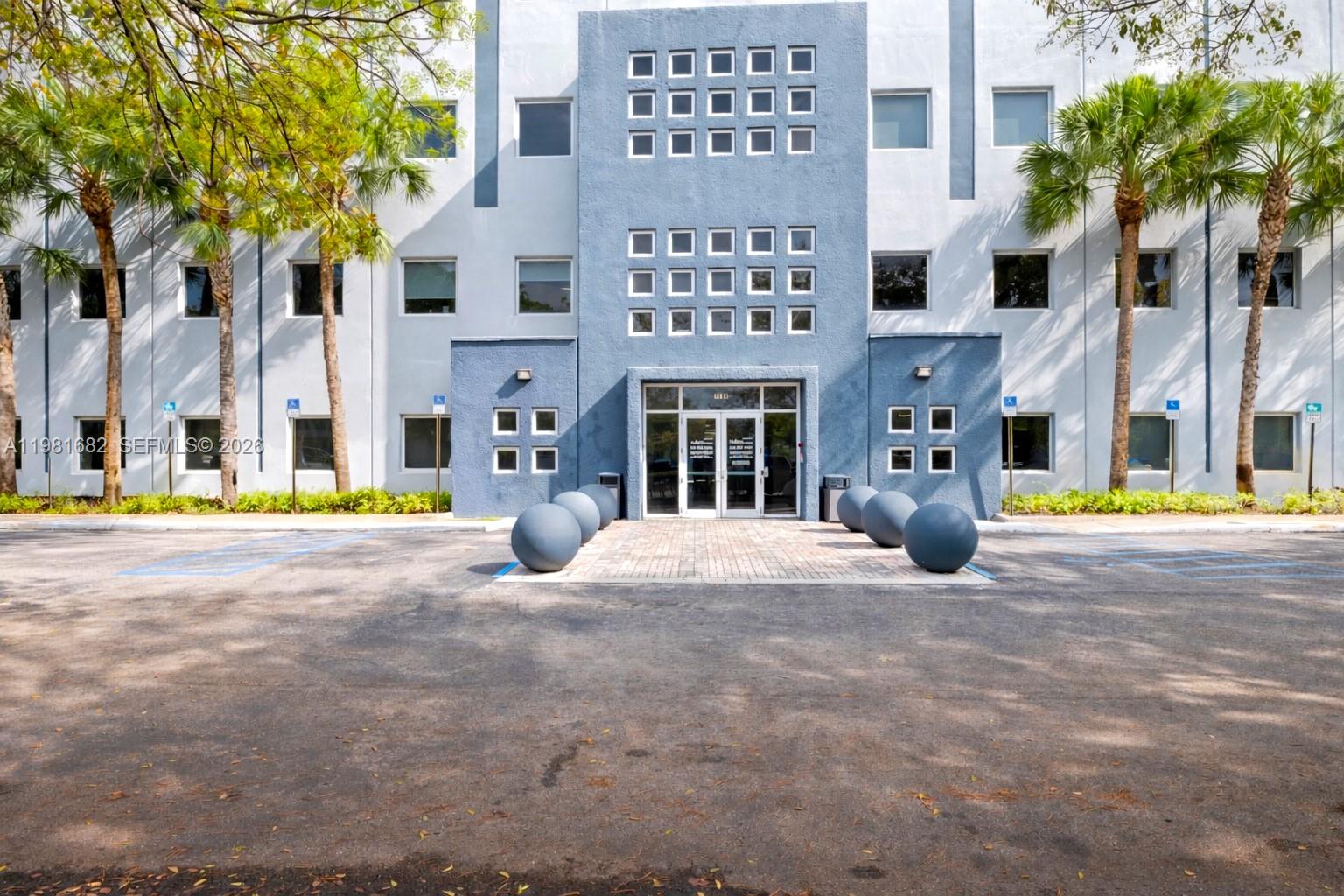 The exterior of a multi-story office building features a blue facade, square windows, and palm trees — 7791 NW 46th St # 306, Doral FL 33166, DORAL, FL