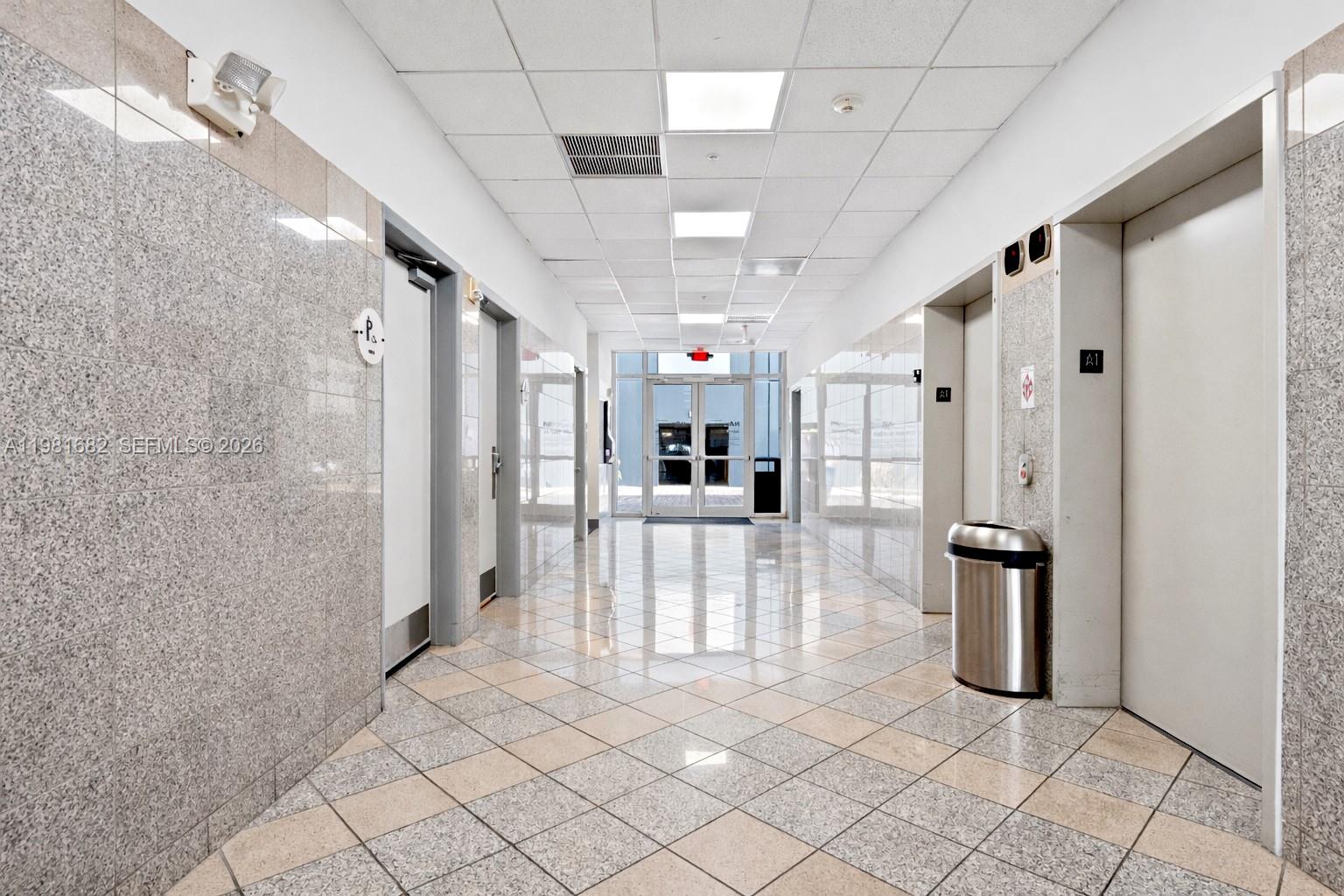 A brightly lit hallway features tiled floors, granite walls, and elevator doors on the right — 7791 NW 46th St # 306, Doral FL 33166, DORAL, FL