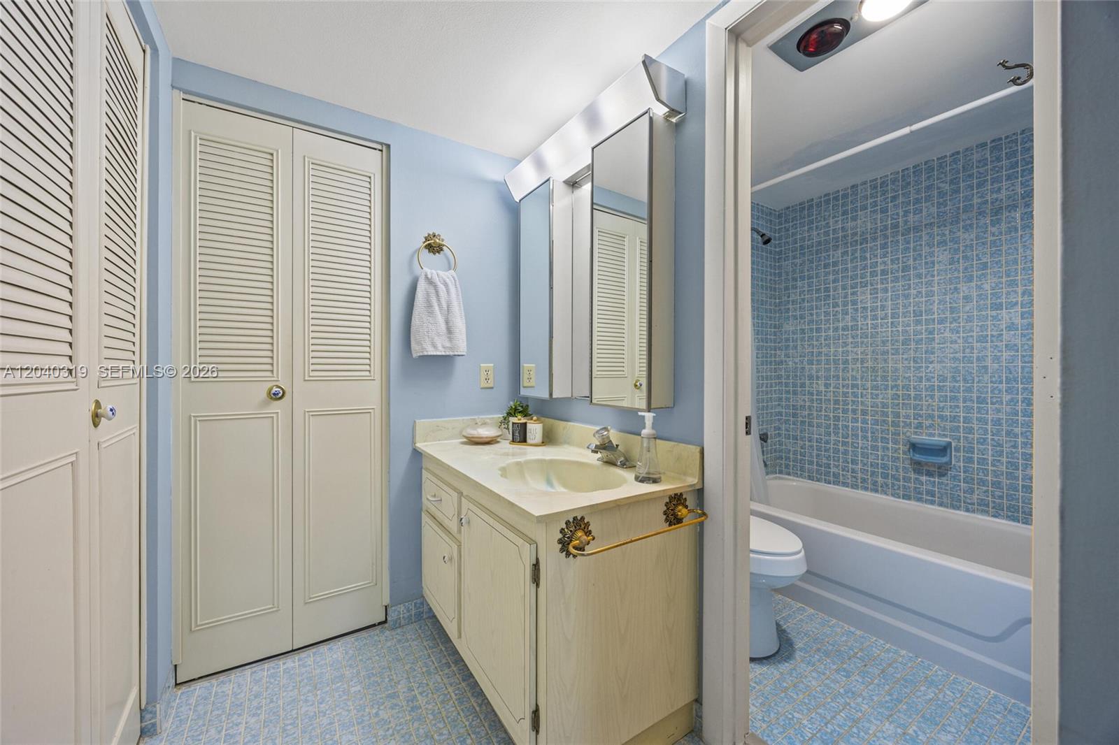 A bathroom features a vanity with a light-colored countertop, blue walls, and a tiled tub — 860 SE 6th Ave # 409, Deerfield Beach FL 33441, DEERFIELD BEACH, FL