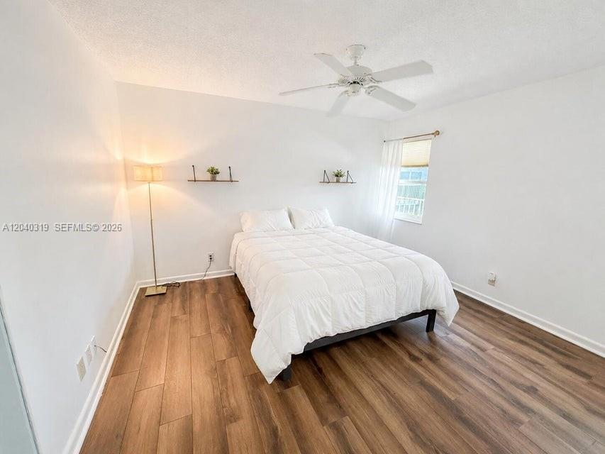 A bedroom features white walls, wood-look flooring, a white bed, and a ceiling fan — 860 SE 6th Ave # 409, Deerfield Beach FL 33441, DEERFIELD BEACH, FL