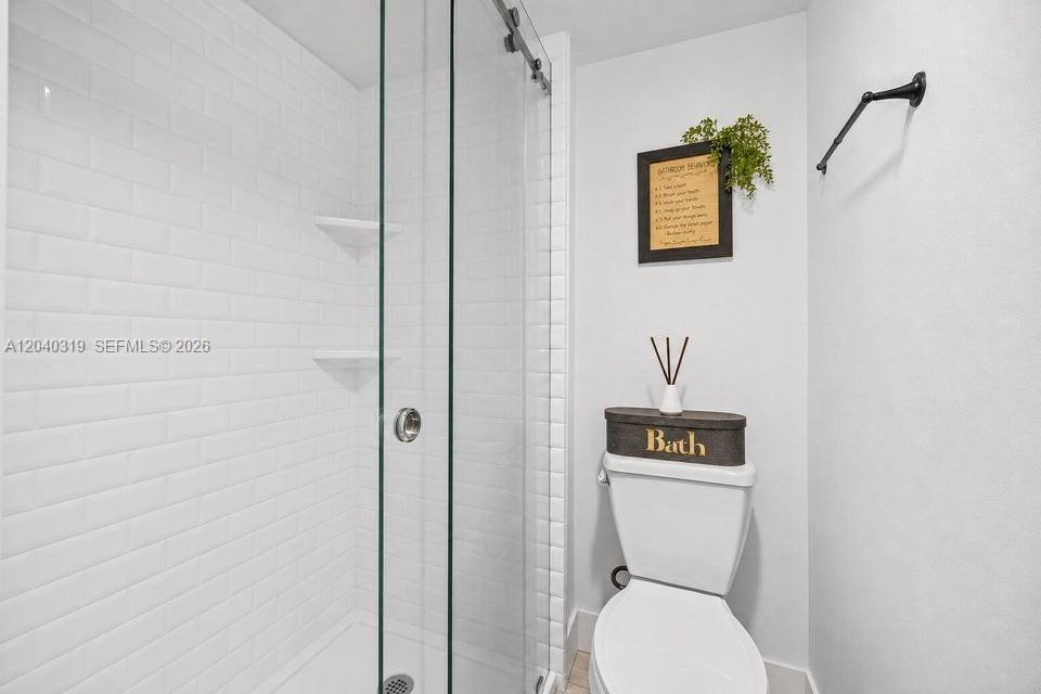 A bathroom features a glass-enclosed shower with white subway tiles and a white toilet — 860 SE 6th Ave # 409, Deerfield Beach FL 33441, DEERFIELD BEACH, FL