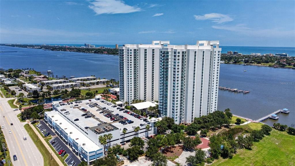 An aerial view shows a tall white residential building next to a parking garage and water — 231 RIVERSIDE DRIVE UNIT 1108-1, HOLLY HILL, FL