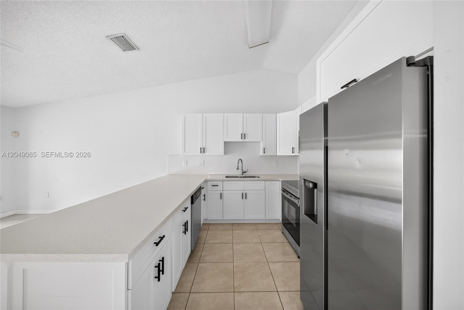 A white kitchen features stainless steel appliances, a breakfast bar, and light-colored tile flooring — 14412 SW 115th St, Miami FL 33186, MIAMI, FL