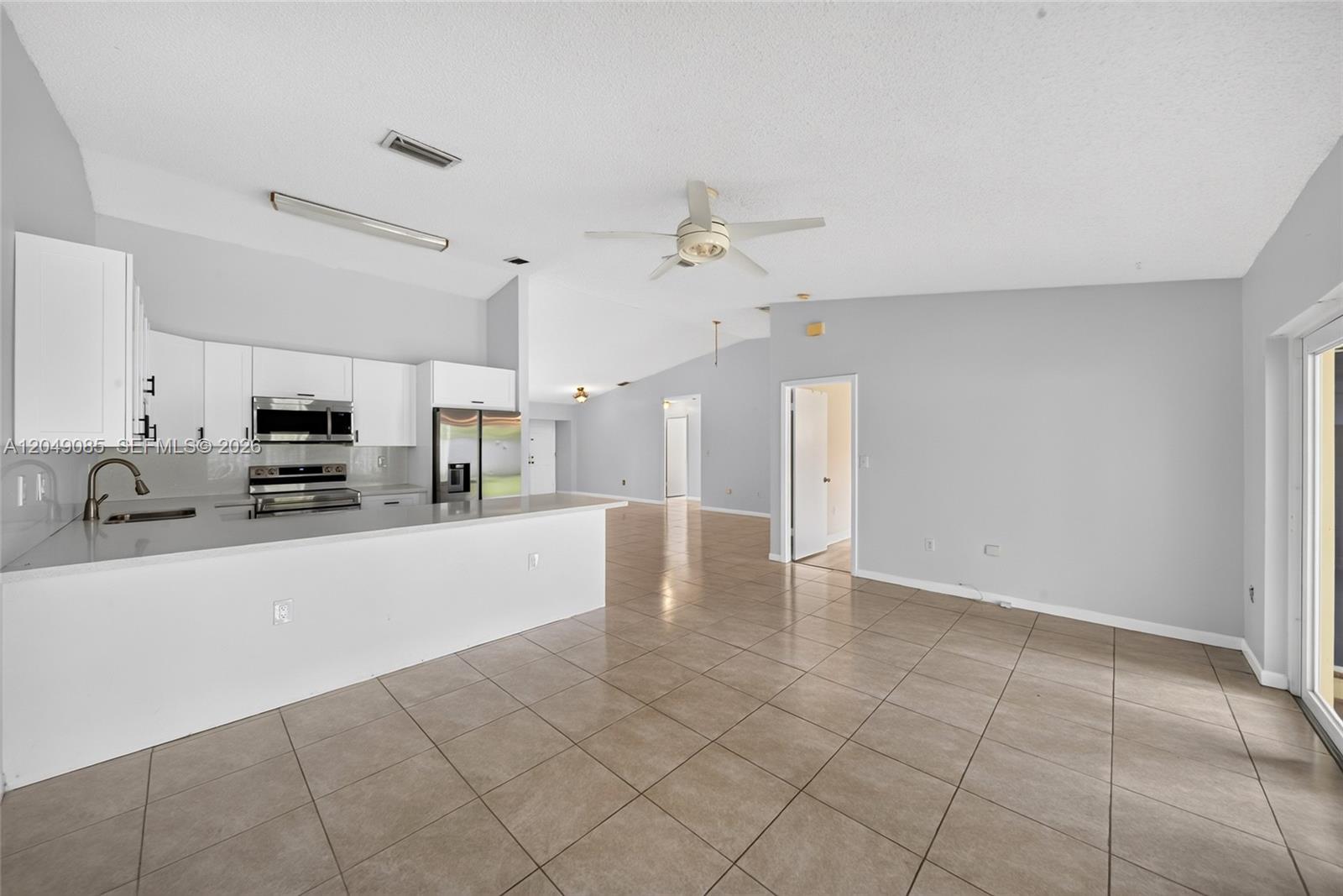 An open-concept kitchen with white cabinets and a breakfast bar overlooks a tiled living area — 14412 SW 115th St, Miami FL 33186, MIAMI, FL