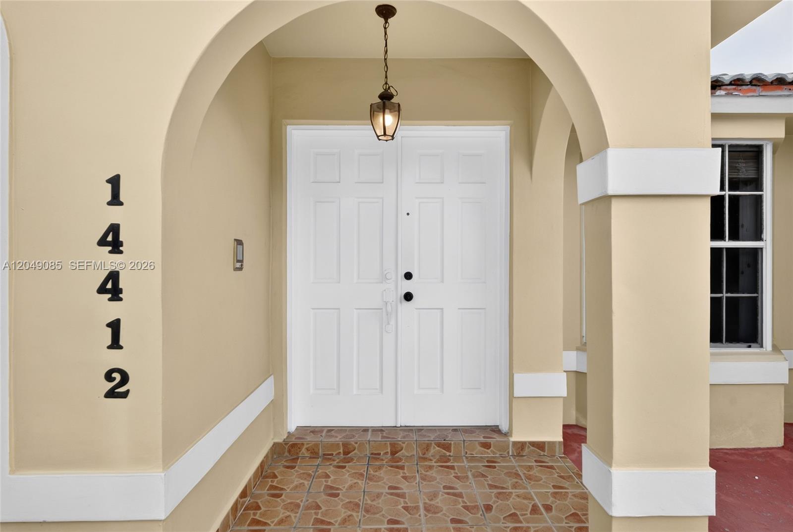 A beige arched entryway features double white doors, a hanging lantern, and tiled flooring — 14412 SW 115th St, Miami FL 33186, MIAMI, FL