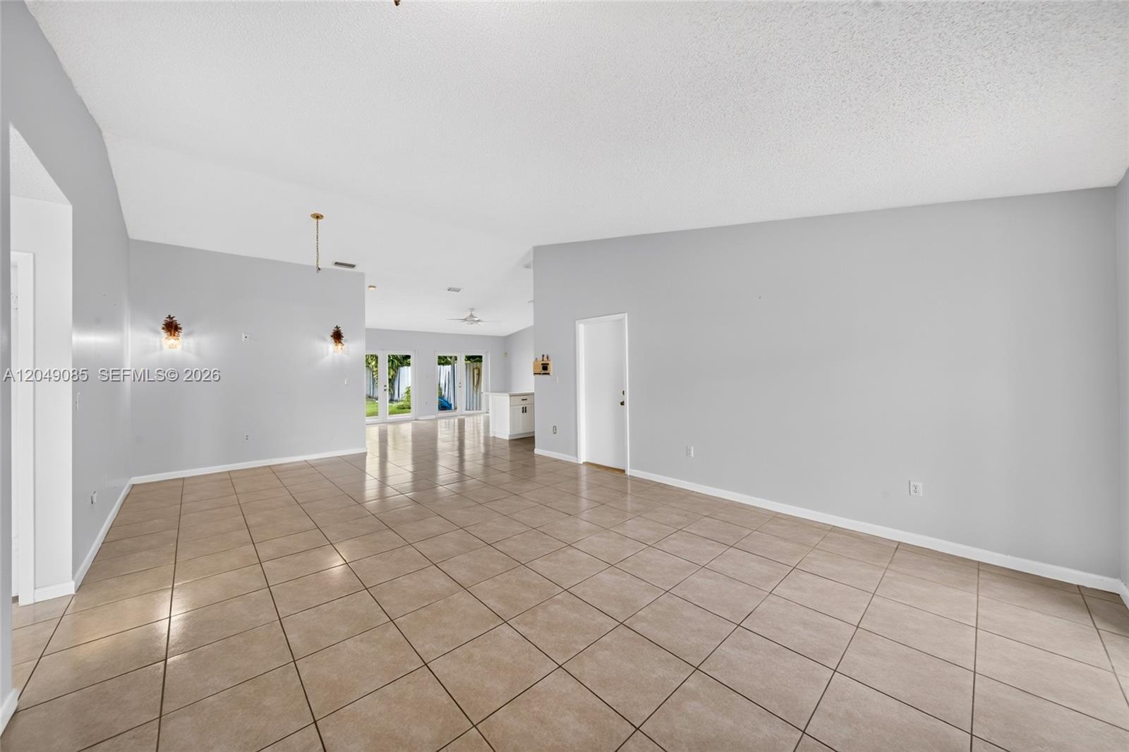 An empty room with light gray walls, tile flooring, and a vaulted ceiling — 14412 SW 115th St, Miami FL 33186, MIAMI, FL