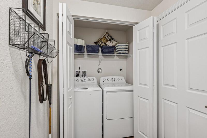 A laundry closet contains a white washer and dryer with storage baskets on a shelf — WEST PALM BEACH, FL