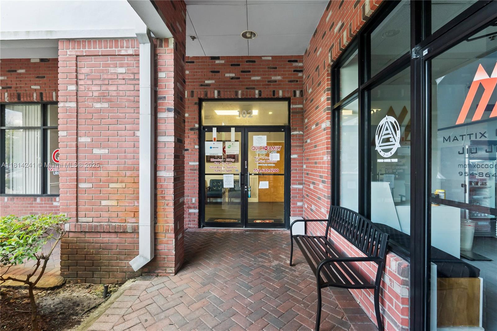 The exterior entrance of a brick building features a glass door and a metal bench — 4301 S Flamingo Rd, Davie FL 33330, DAVIE, FL