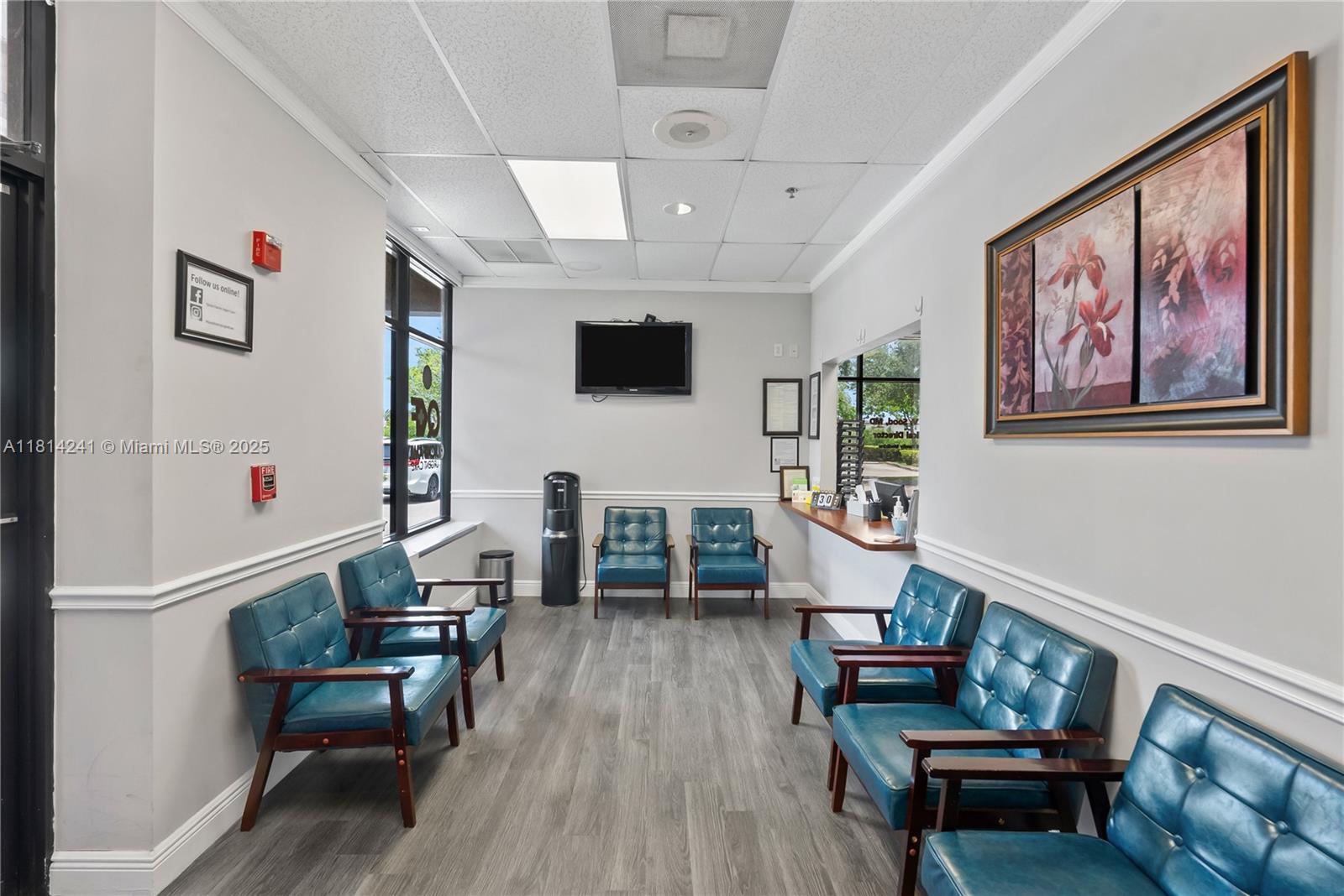 A waiting room features blue leather chairs, wood-look flooring, a television, and a reception window — 4301 S Flamingo Rd, Davie FL 33330, DAVIE, FL