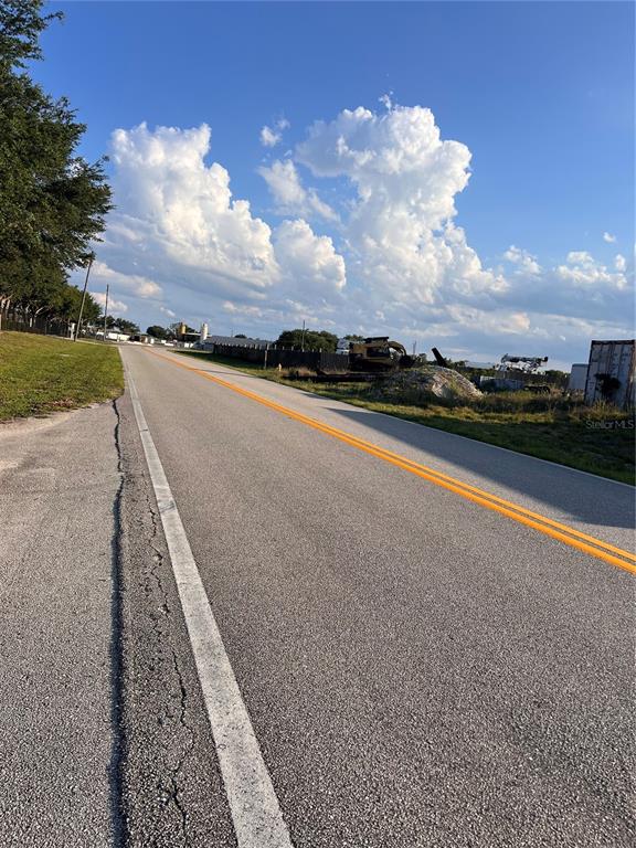 A paved road with double yellow lines runs past a grassy lot and construction equipment — 7513 S GEORGE BOULEVARD, SEBRING, FL