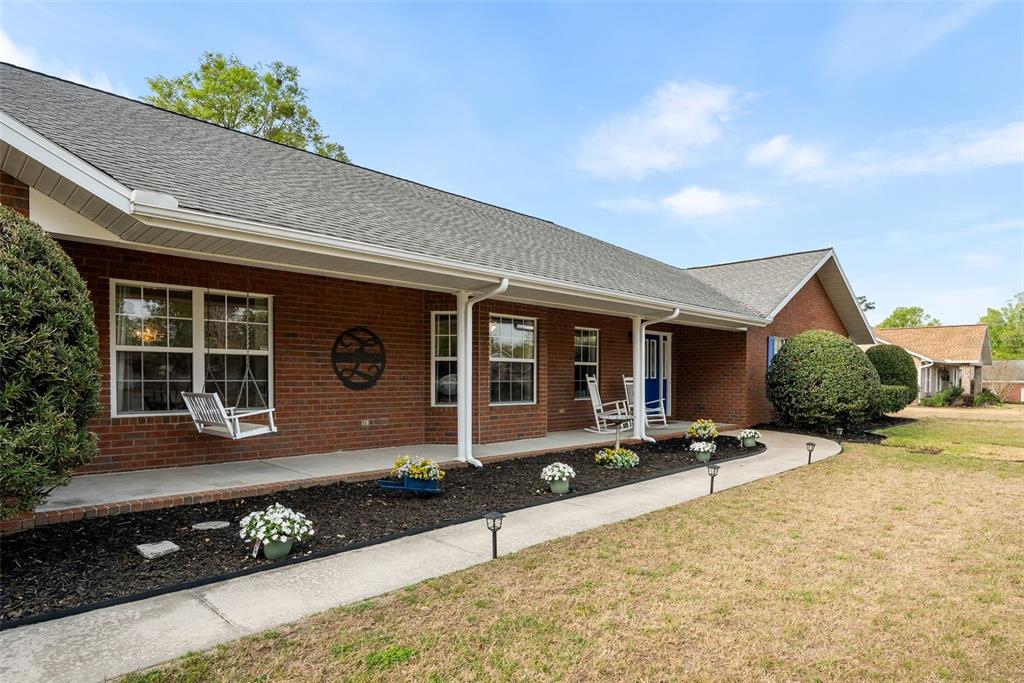 A brick ranch-style house features a covered front porch with a swing and rocking chairs — 244 SW LOBLOLLY PLACE, LAKE CITY, FL