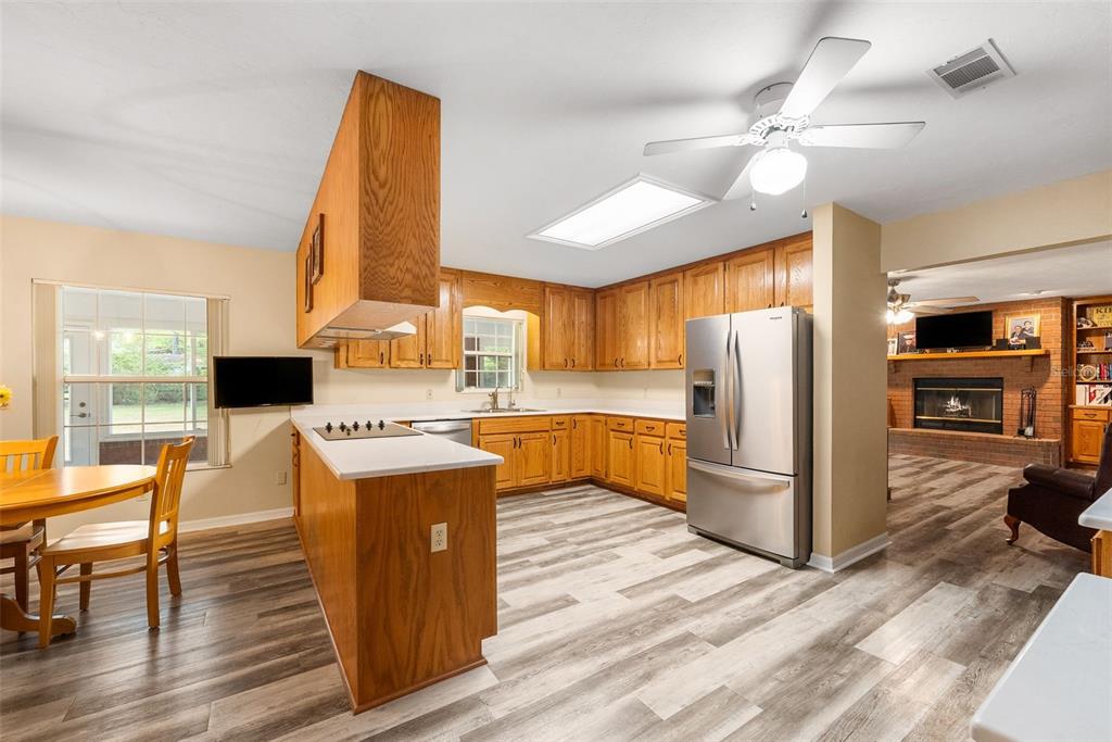 A kitchen with wood cabinets, stainless steel appliances, and wood-look flooring opens to a living area — 244 SW LOBLOLLY PLACE, LAKE CITY, FL
