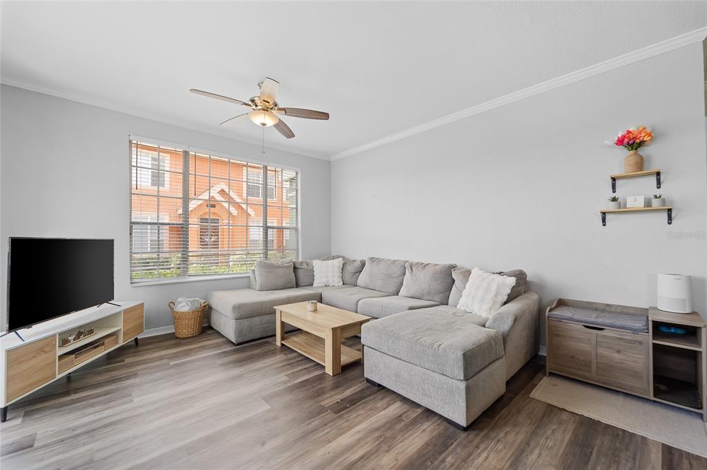 A living room features a grey sectional sofa, wood-look flooring, and a television on a console — 10518 WHITE LAKE COURT UNIT 10518, TAMPA, FL