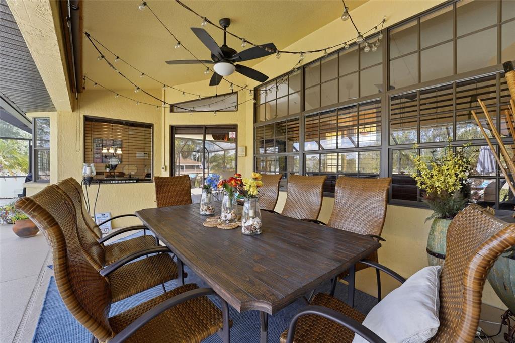 A covered patio features a wooden dining table with wicker chairs and string lights — 3420 S SUMTER BOULEVARD, NORTH PORT, FL