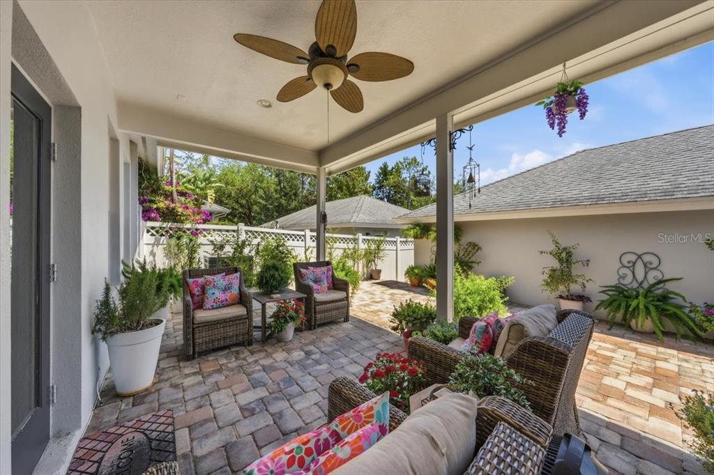A covered patio features wicker furniture, a ceiling fan, and potted plants on a paver floor — 9606 ROYCE DRIVE, TAMPA, FL