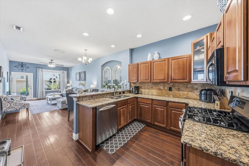 A kitchen with wood cabinets and granite countertops opens into a living room with hardwood floors — 9606 ROYCE DRIVE, TAMPA, FL