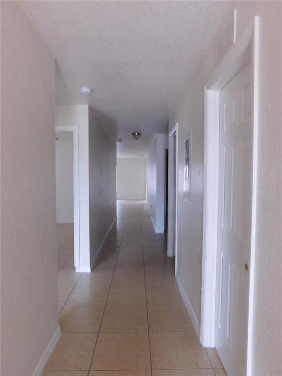 A long hallway with light-colored tile flooring leads toward an open room in the distance — 756 CAMEL COURT, KISSIMMEE, FL