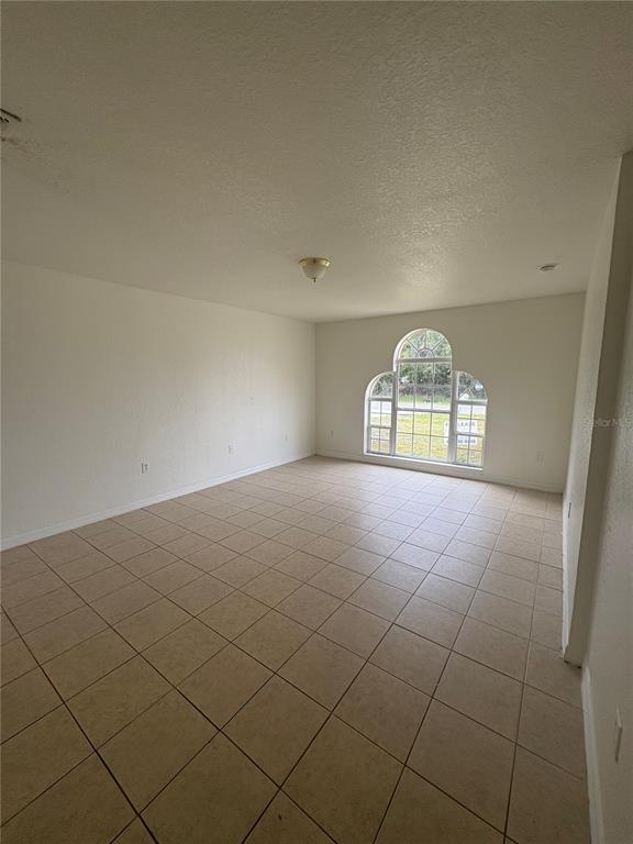 An empty room with beige tile flooring, white walls, and an arched window — 756 CAMEL COURT, KISSIMMEE, FL