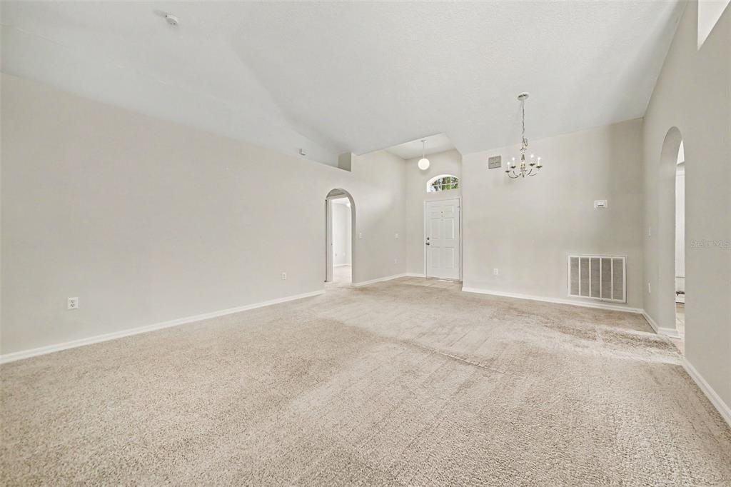A living room with beige carpet, vaulted ceilings, an arched doorway, and a chandelier — 2122 AITKIN LOOP, LEESBURG, FL