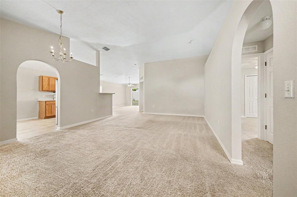 A spacious living room with beige carpet, arched doorways, and a view into the kitchen — 2122 AITKIN LOOP, LEESBURG, FL