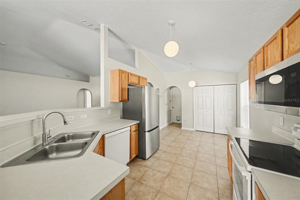 A kitchen with light countertops, wood cabinets, stainless steel appliances, and tile flooring — 2122 AITKIN LOOP, LEESBURG, FL