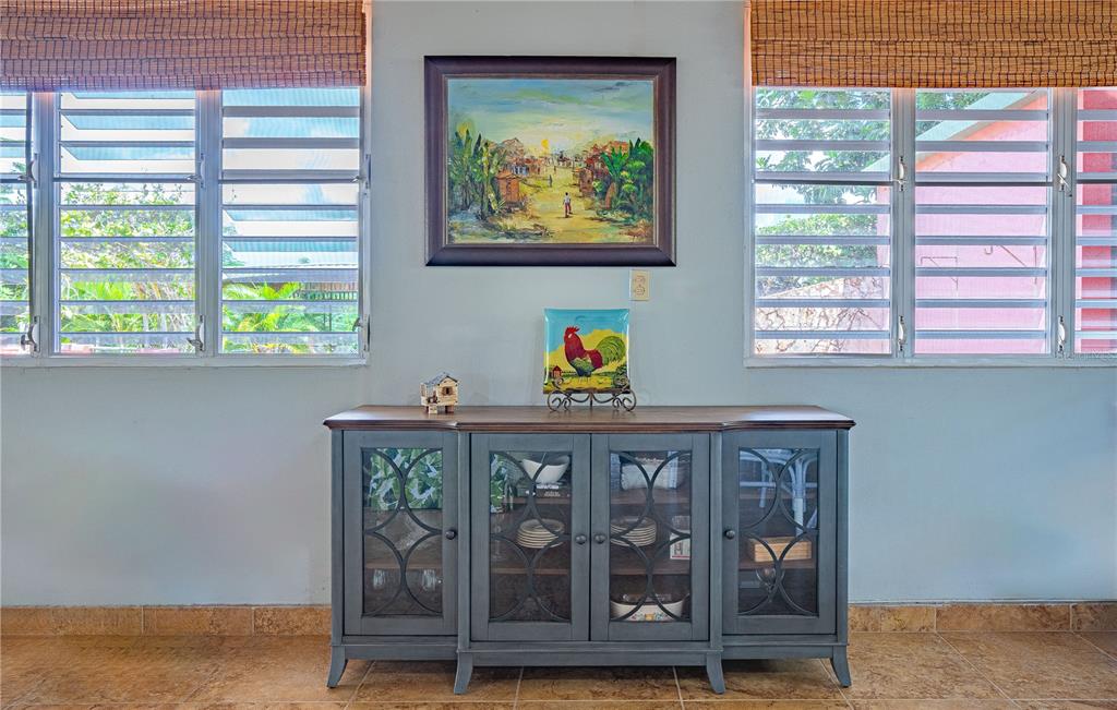 A gray wooden sideboard sits against a light blue wall between two windows with blinds — 2 #8 URBANIZABLE. VILLA SOÑDA, TRUJILLO ALTO, PR