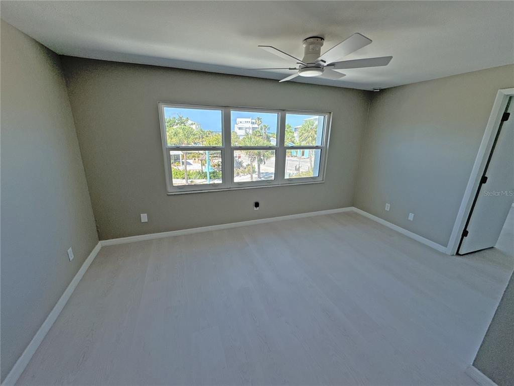 An empty bedroom features light wood flooring, gray walls, a ceiling fan, and large windows — 1285 GULF BOULEVARD UNIT 5, ENGLEWOOD, FL