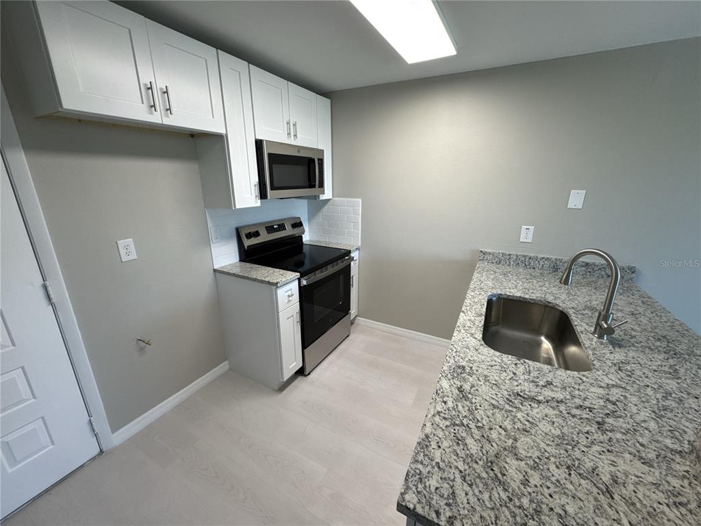 A kitchen features white cabinets, stainless steel appliances, and granite countertops with a sink — 1285 GULF BOULEVARD UNIT 5, ENGLEWOOD, FL