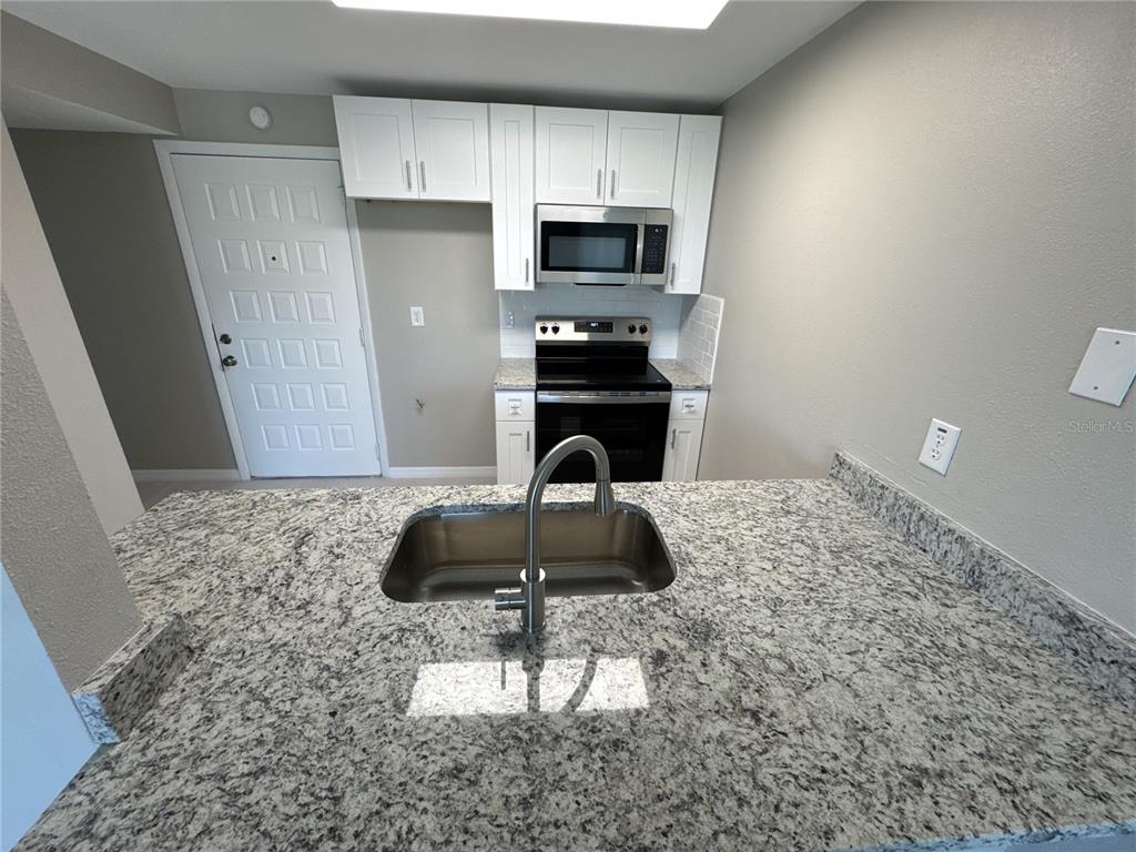 A kitchen features white cabinets, granite countertops, stainless steel appliances, and a sink island — 1285 GULF BOULEVARD UNIT 5, ENGLEWOOD, FL