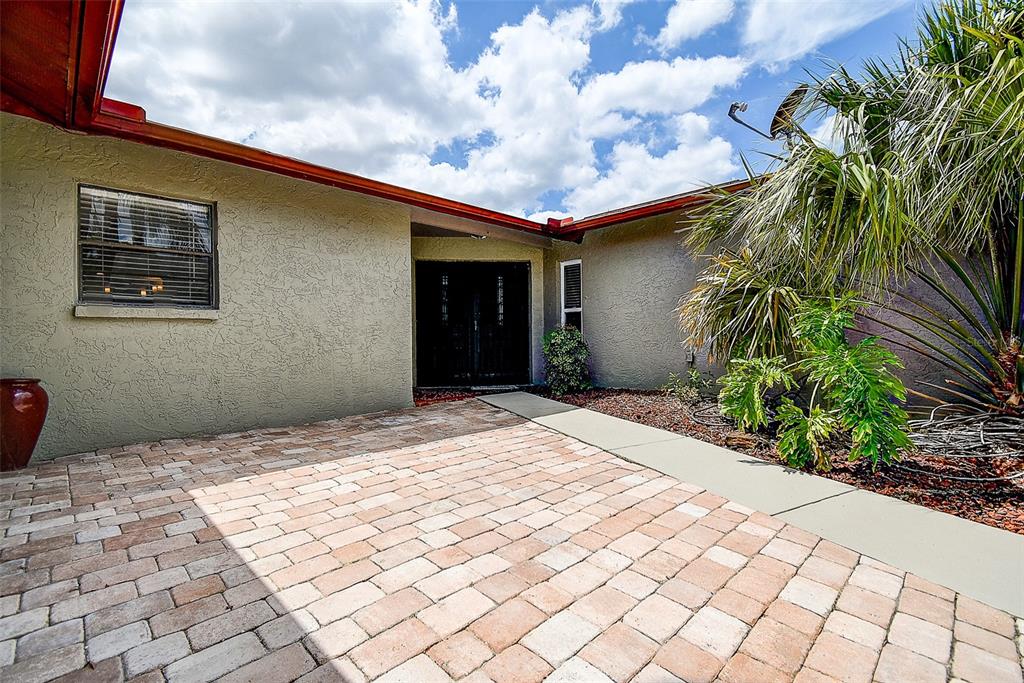 A paved courtyard leads to the dark double front doors of a stucco house — 7556 HIGH PINES COURT, PORT RICHEY, FL