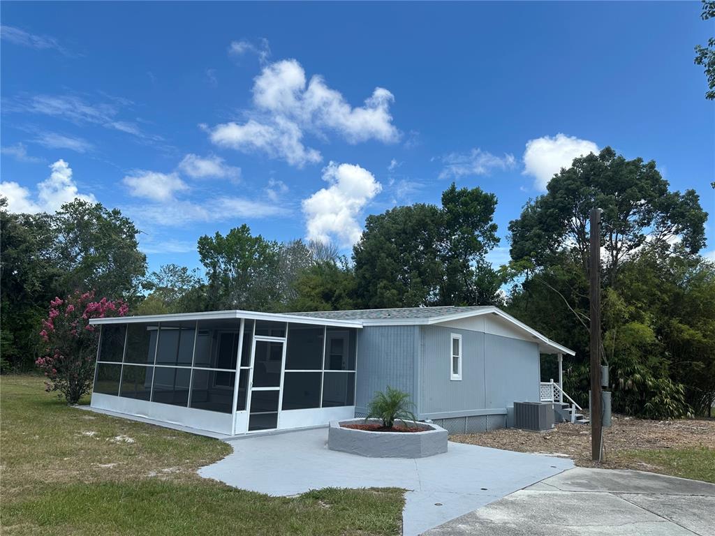A light blue mobile home features a screened-in porch and a small concrete patio area — 18021 APPLEJACK COURT, SPRING HILL, FL